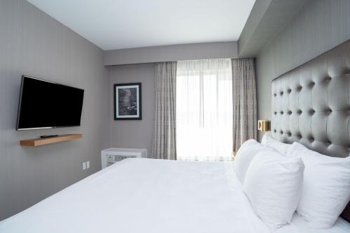 a bedroom with a large white bed with a flat screen tv at Sandman Hotel Hamilton in Hamilton