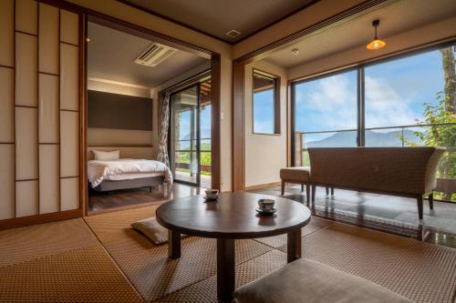 a room with a table and a bed and windows at Kusayane no yado Ryunohige in Yufu