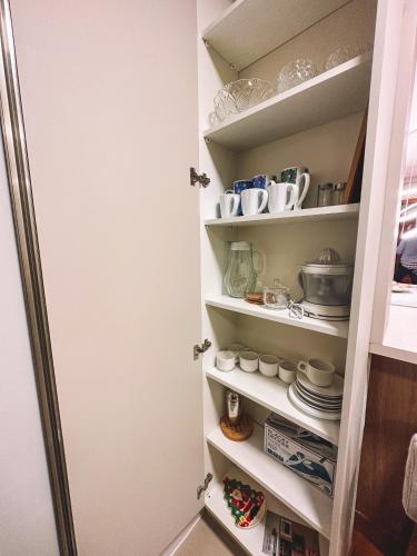a kitchen pantry with white shelves and dishes at Apto a 3 minutos da Rua Coberta de Gramado in Gramado
