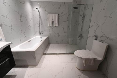 ein weißes Badezimmer mit einer Badewanne, einem WC und einem Waschbecken in der Unterkunft J&V Hotel and Resort in Apaleng