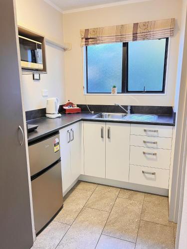 a kitchen with white cabinets and a sink and a window at Kingswood Manor Motel in Whangarei