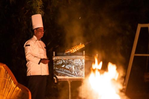 a chef standing next to a grill with fire at Tiger Machan in Sawāi Mādhopur