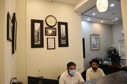 two men wearing masks in a restaurant with a clock on the wall at Hayyat Luxury Hotel Apartments in Lahore