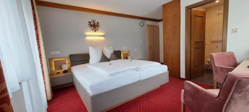 a bedroom with a large white bed and two chairs at Haus Tirol Appartements in Ried im Oberinntal
