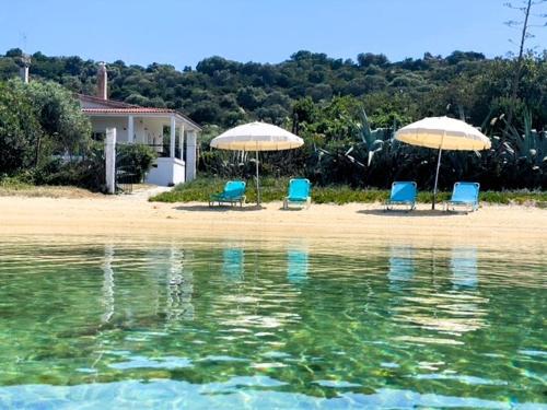 3 Stühle und Sonnenschirme am Strand neben dem Wasser in der Unterkunft Casa Santa Agua in Amolianí