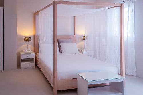 a white bedroom with a canopy bed and a table at Milos Bay Suites in Adamas
