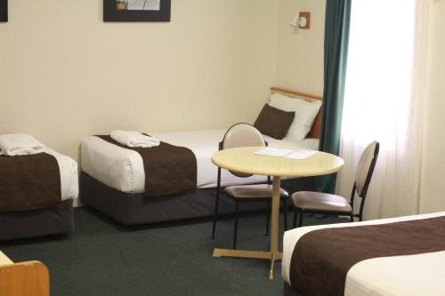 a room with two beds and a table and chairs at Mid City Motor Inn Singleton in Singleton