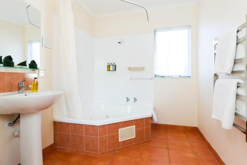 a bathroom with a bath tub and a sink at Elliotts Kapiti Coast Motor Lodge in Paraparaumu Beach