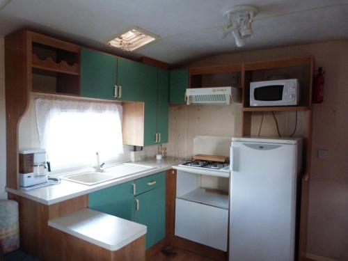 a small kitchen with green cabinets and a white refrigerator at camping la rivière in Vabre-Tizac