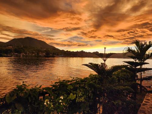 a sunset over a body of water with palm trees at PURNAMA BALIGE HOTEL in Balige