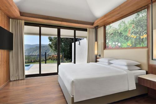 a bedroom with a white bed and a large window at Courtyard by Marriott Mahabaleshwar in Mahabaleshwar
