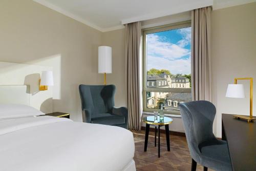 a hotel room with a bed and two chairs and a window at Sheraton Offenbach Hotel in Offenbach