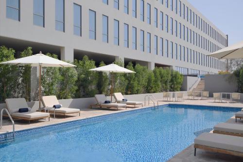 a swimming pool with chairs and umbrellas next to a building at Delta Hotels by Marriott Dubai Investment Park in Dubai
