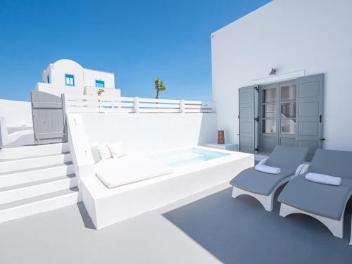 a white bedroom with a bed and two chairs at Anthemis Suites in Imerovigli
