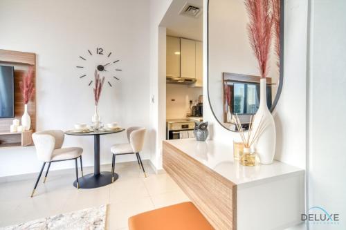 a living room with a table and chairs and a clock on the wall at Sleek Studio at UNA Town Square Dubailand by Deluxe Holiday Homes in Dubai