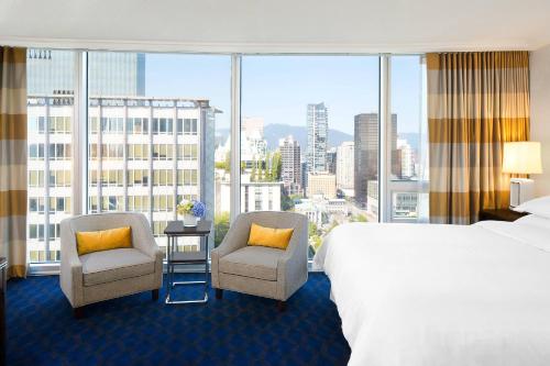 a hotel room with a bed and two chairs and a large window at Sheraton Vancouver Wall Centre in Vancouver