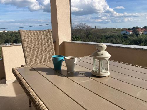 a wooden table with two cups and a lantern on a balcony at Apartman Hmelina in Vrsi