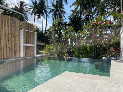 a man sitting on the edge of a swimming pool at Lala Salama Backpacker in Teluk Nara