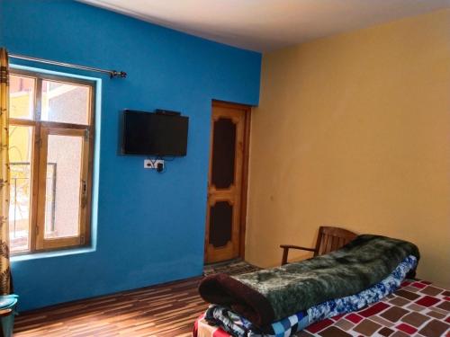 a room with a blue wall with a bed and a tv at Noor Guest House in Leh