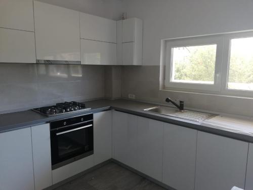 a kitchen with white cabinets and a sink and a window at Casa luminoasa cu parcare gratuita la proprietate in Dumbrăviţa