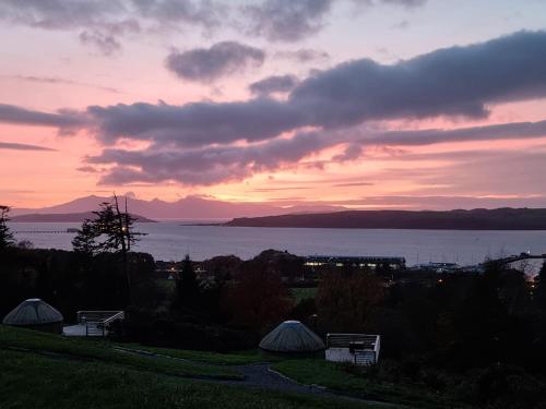 a sunset over a lake with tents in a field at Kelburn Yurts in Fairlie