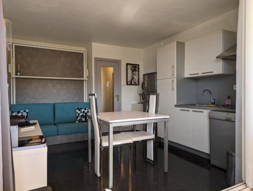 une petite cuisine avec une table et un canapé bleu dans l'établissement Studio Héliopolis K Int. Village Natu, Clim, Park., au Cap d'Agde