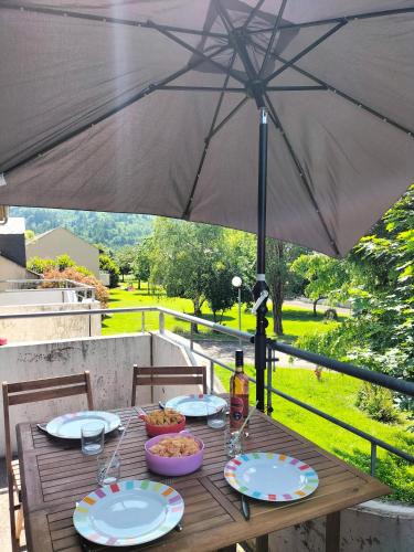 une table en bois avec des assiettes de nourriture et un parasol dans l'établissement T2 avec piscine-Le family 67, à Pierrefiche