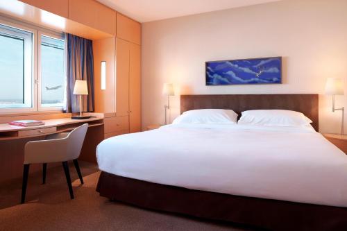 a hotel room with a large white bed and a desk at Sheraton Paris Charles de Gaulle Airport Hotel in Roissy-en-France