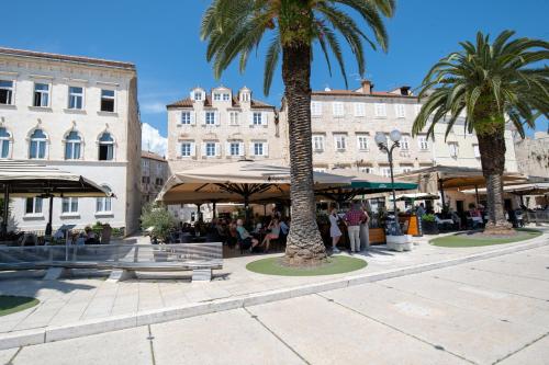 a street with palm trees and people sitting under umbrellas at Luxury Rooms "Kaleta" in Trogir