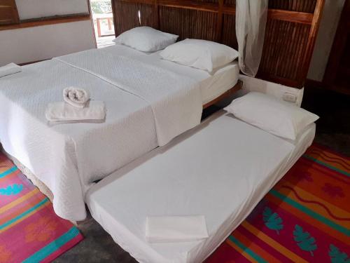 two beds in a room with white sheets and towels at Las Cabañas del Rio in Minca