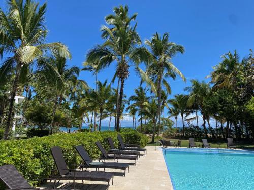 a row of chairs next to a swimming pool with palm trees at Stunning Beachfront Condo With Private Beach, Las Terrenas-El Limón in El Limón