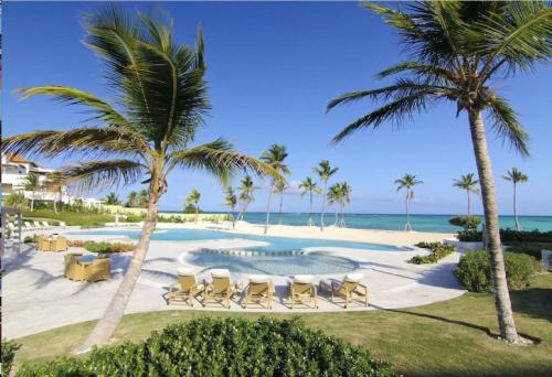 un complexe avec une piscine, des palmiers et l'océan dans l'établissement New! Beachfront Lux Condo With Private Jacuzzi, à Punta Cana