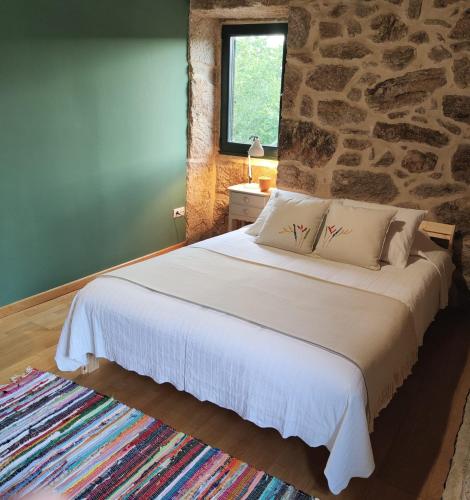 a bedroom with a white bed with a stone wall at Casa Ribadil in Crecíente
