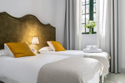 2 łóżka w pokoju z białymi i żółtymi poduszkami w obiekcie San Buenaventura Apartment 1 w Sewilli