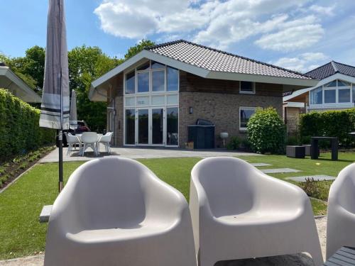 two white chairs and an umbrella in front of a house at Strandvilla met sauna in Westerhaar-Vriezenveensewijk