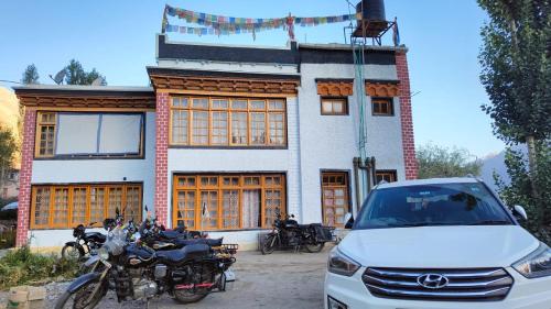 une voiture blanche garée devant un immeuble avec des motos dans l'établissement Zambala guest house, à Leh