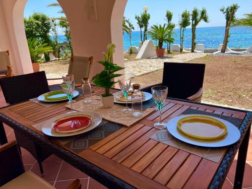 a wooden table with plates and wine glasses on it at Casale fronte mare - villa with swimming pool in front of the beach in Porto Columbu - Perdʼe Sali
