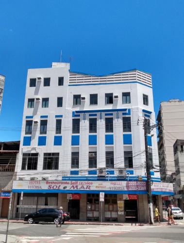 a white building on a street corner with a car in front at Hotel Sol e Mar in Vitória