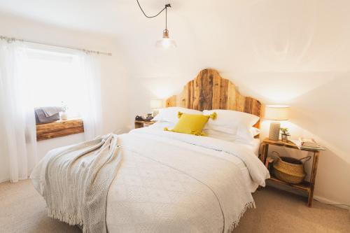 a bedroom with a white bed with a wooden headboard at The Bee Cottage Rutland - 17th century thatched. in Cottesmore