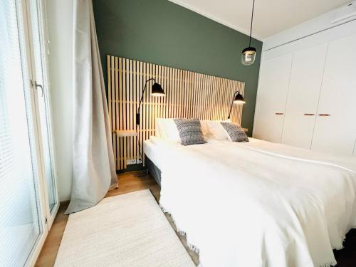 a bedroom with a large white bed and a green wall at Uusi upea kaksio Tampereen ytimessä, pysäköinti, iso lasitettu parveke in Tampere