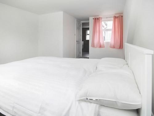 ein weißes Bett in einem weißen Schlafzimmer mit rosa Vorhängen in der Unterkunft Sahara Rose in East Grinstead