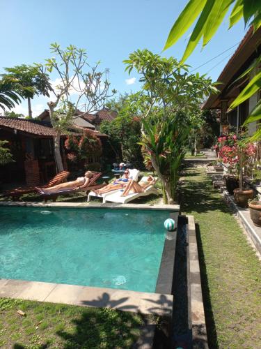 a pool with two people laying on chairs in a yard at Werkudara Guest House in Ubud