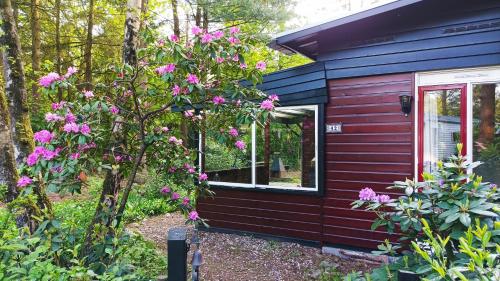 a red house with a window and pink flowers at Bosbungalow de Eekhoorn in Nunspeet