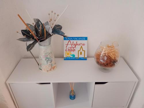 a white cabinet with a book and a vase with flowers at Alghero d'Estate in Alghero