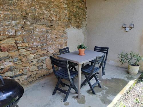 a table with four chairs and a stone wall at L'étape de la Tour in Grand-Fougeray