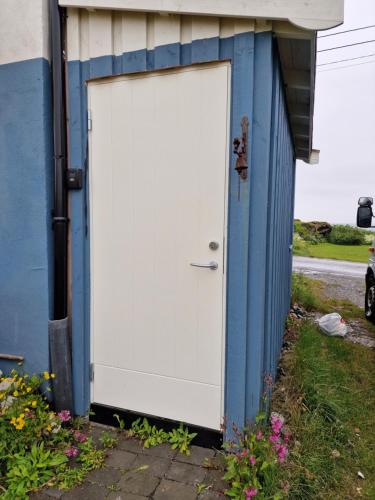 una puerta blanca en el lateral de un edificio azul en Liten leilighet i Berlevåg, en Berlevåg