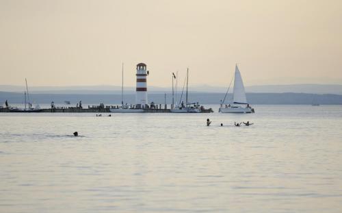 a group of people swimming in the water with a lighthouse at Seewirt & Haus Attila in Podersdorf am See