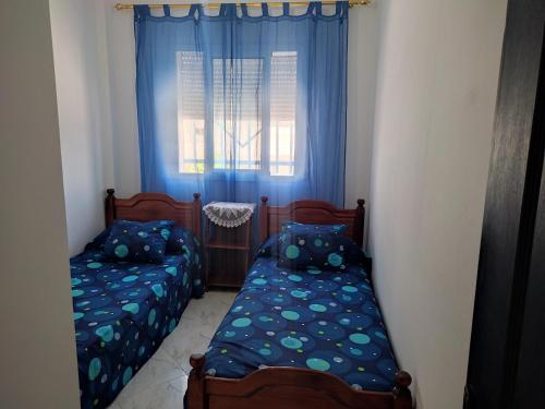 a bedroom with two beds and a window with blue curtains at Peaceful Apartment in Al Hoceïma