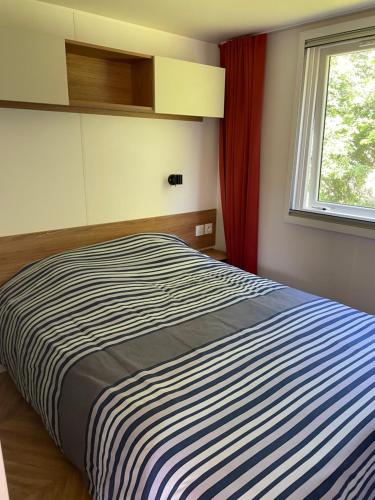 1 dormitorio con cama de rayas y ventana en Mobil-home 3 chambres dans camping *** avec piscine, en Plouézec