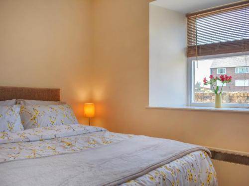 a bedroom with a bed and a window with a vase of flowers at Hatters Croft in Cockermouth